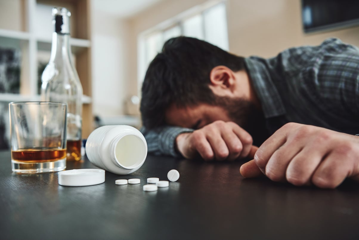 Alcoholism and drug addiction are killer of mental and physical health. Drunk man at table with alcohol and drugs. Alcoholism concept